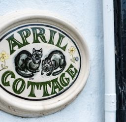A ceramic sign with two cats and green text reading April Cottage on a white wall at April Cottage in Port Isaac