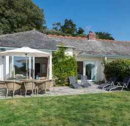 A garden patio with a dining table and umbrella and lounge chairs in front of a white house at Carn Du 1 in Rock