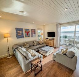 A living room with sofas a wooden cabinet and a large sliding door opening to an outdoor dining area at Carn Du 1 in Rock