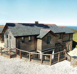 A wooden house with a fenced gravel area and a stone patio near the coast at Ossco in Polzeath