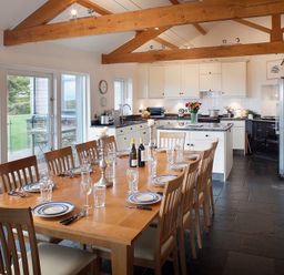A kitchen and dining area with a wooden dining table set for eight and white cabinets at Ossco in Polzeath