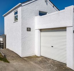 Exterior view of a white building with a garage door and signs that say The Folly and Signal Post at The Folly in Port Isaac