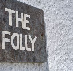 A metal sign with the words The Folly mounted on a white textured wall at The Folly in Port Isaac