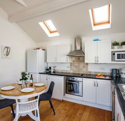 A kitchen with a round dining table set for four and white cabinets at The Folly in Port Isaac