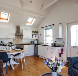 A kitchen with white cabinets and a dining table with chairs and a bouquet of flowers on the table at The Folly in Port Isaac
