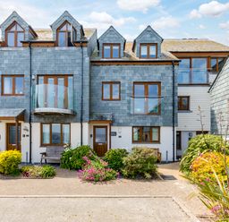 A row of houses with slate roofs and wooden windows with flower beds and benches outside at Rock Lobster in Port Isaac