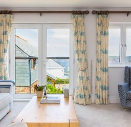 A living room with sofas a wooden coffee table and a view of buildings and sea through glass doors at Rock Lobster in Port Isaac