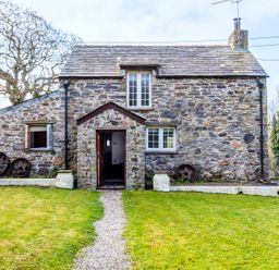 A stone cottage with a gravel path leading to an open wooden door and lawn at Dingles Cottage in Rock