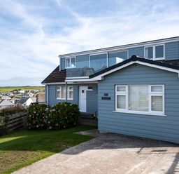 A blue two-story house with a glass balcony and driveway at Atlantis in Polzeath