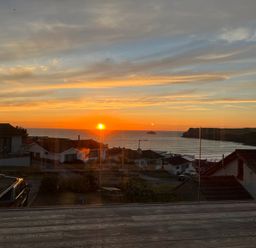 A sunset view over houses and the sea with birds flying above at Atlantis in Polzeath