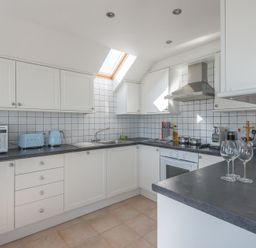 A kitchen with white cabinets black countertops a microwave toaster kettle stove oven and a skylight at Polmorla in Polzeath