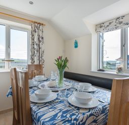 A dining area with a table set with white bowls and glasses in front of windows at Polmorla in Polzeath
