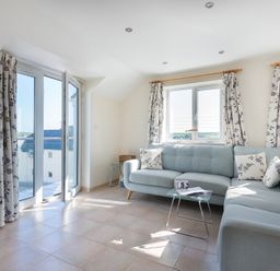 A living room with light blue sofa and floral curtains near windows and glass door at Polmorla in Polzeath
