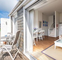 An open patio door showing a balcony with chairs and a table and an interior with a dining table and chairs a sofa and a coffee table at Slipway 12 in Rock