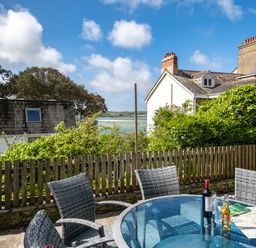An outdoor patio area with a glass table and four chairs overlooking a wooden fence and neighboring houses at Slipway 12 in Rock