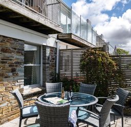 An outdoor patio with a round glass table and six wicker chairs next to a stone wall at Slipway 12 in Rock