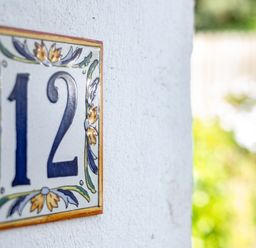 A ceramic house number 12 plaque on a white wall with a blurred garden background at Slipway 12 in Rock