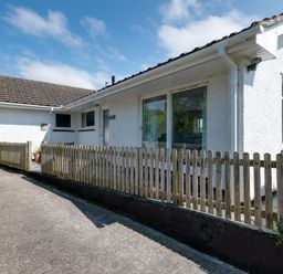 Exterior view of a white house with tiled roof and wooden fence along a driveway at Tremay Rock