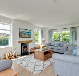 A living room with two gray sofas a wooden coffee table a rug a fireplace and windows with curtains at Tremay in Rock