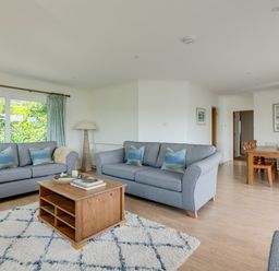 A living room with two gray sofas a wooden coffee table a floor lamp and a dining area with a wooden table and chairs at Tremay in Rock