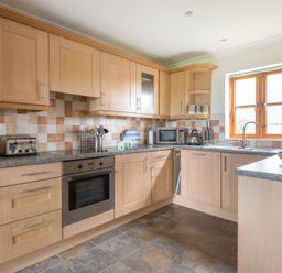 A kitchen with wooden cabinets countertop microwave toaster oven and window at Lundy Cottage in Rock