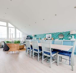 A dining area with a long table and chairs and a seating area with sofas and green cushions at The Point in Polzeath