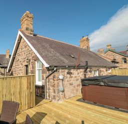 An outdoor deck area with a hot tub wooden fencing and stone houses in the background at Cheviot Hills in Wooler