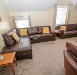 A living room with brown leather sofas and yellow cushions two wooden side tables with lamps and windows with beige curtains at Cheviot Hills in Wooler