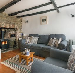 A living room with a stone fireplace grey couches wooden coffee table and striped rug at Cloam Cottage in Port Isaac