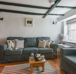 A living room with a grey sofa and armchair a small wooden coffee table and window seat at Cloam Cottage in Port Isaac