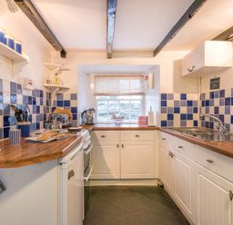 A kitchen with white cabinets wooden countertops blue and white tiled walls and a window at Cloam Cottage Port Isaac