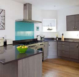 A kitchen with gray cabinets a countertop stove a green bowl of fruit and a sink at The Beach Hut in Polzeath