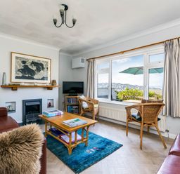 A living room with red leather sofas a wooden coffee table a blue rug and a window showing an outdoor view at Bella Vista in Polzeath