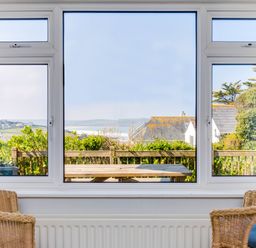 A view through three pane windows showing a wooden picnic table outside and houses with greenery in the background at Bella Vista in Polzeath