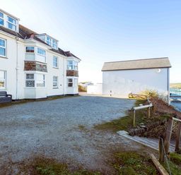 An outdoor space with white buildings a gravel area and wooden stairs leading down at Pinewood Flat 5 in Polzeath