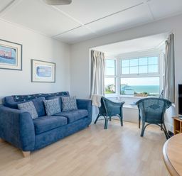 A living room with a blue sofa and two chairs by a window with ocean view at Pinewood Flat 5 in Polzeath