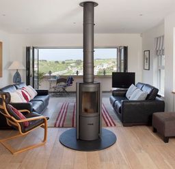 A living room with two black sofas a wood burning stove and a folding door leading to a balcony at Kellan in Polzeath