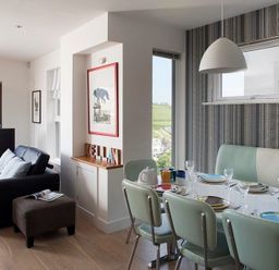 A dining area with a table set with plates and glasses next to a living space with a sofa and television at Kellan in Polzeath