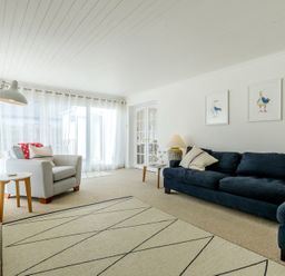 A living room with a blue sofa and armchair with pillows a floor lamp and framed bird pictures at The Moorings in Rock