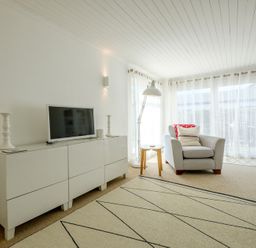 A living room with a white cabinet holding a television two candlesticks a chair with pillows a small round table and a floor lamp at The Moorings in Rock