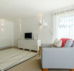 A living room with a striped armchair a floor lamp a white cabinet a television and a rug at The Moorings in Rock