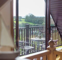 A balcony with a round table set with a vase of flowers and wine glasses viewed through a glass door at Sandy Hills 8 in Rock