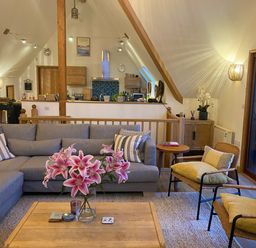 A living room with a gray sectional sofa pink flowers on a wooden coffee table and wooden chairs at Sandy Hills 8 in Rock