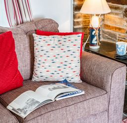 A sofa with cushions and an open book next to a side table with a lamp and a cup at St Michaels in Rock