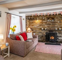 A living room with a sofa red and white cushions a wood burning stove and stone wall at St Michaels in Rock