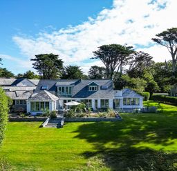 A large house with multiple windows and patios surrounded by a green lawn and tall trees at Greystones in Daymer Bay