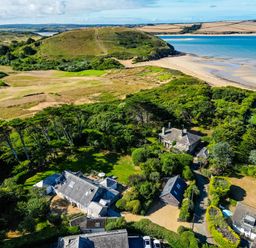 An aerial view of several houses surrounded by trees near a beach and a grassy hill at Greystones in Daymer Bay