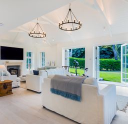 A living room with white sofas a fireplace a television and open doors to a garden at Greystones in Daymer Bay