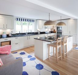 A kitchen with white cabinets a black countertop an island with two wooden stools and a grey sofa with striped cushions at Cherrytrees Rock