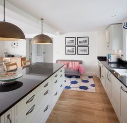 A kitchen with black countertops white cabinets a dining table and a small couch with striped cushions at Cherrytrees in Rock